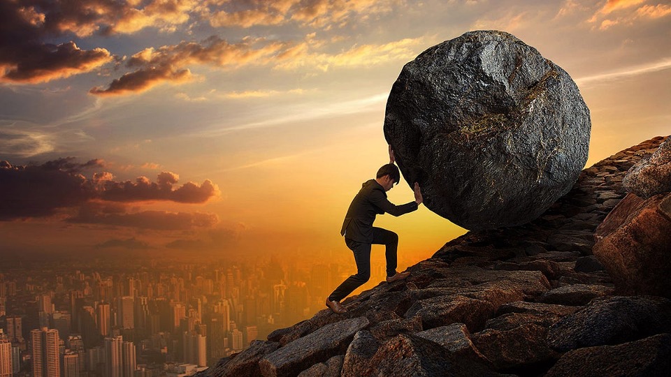 Man pushing a boulder up a mountain at sunset